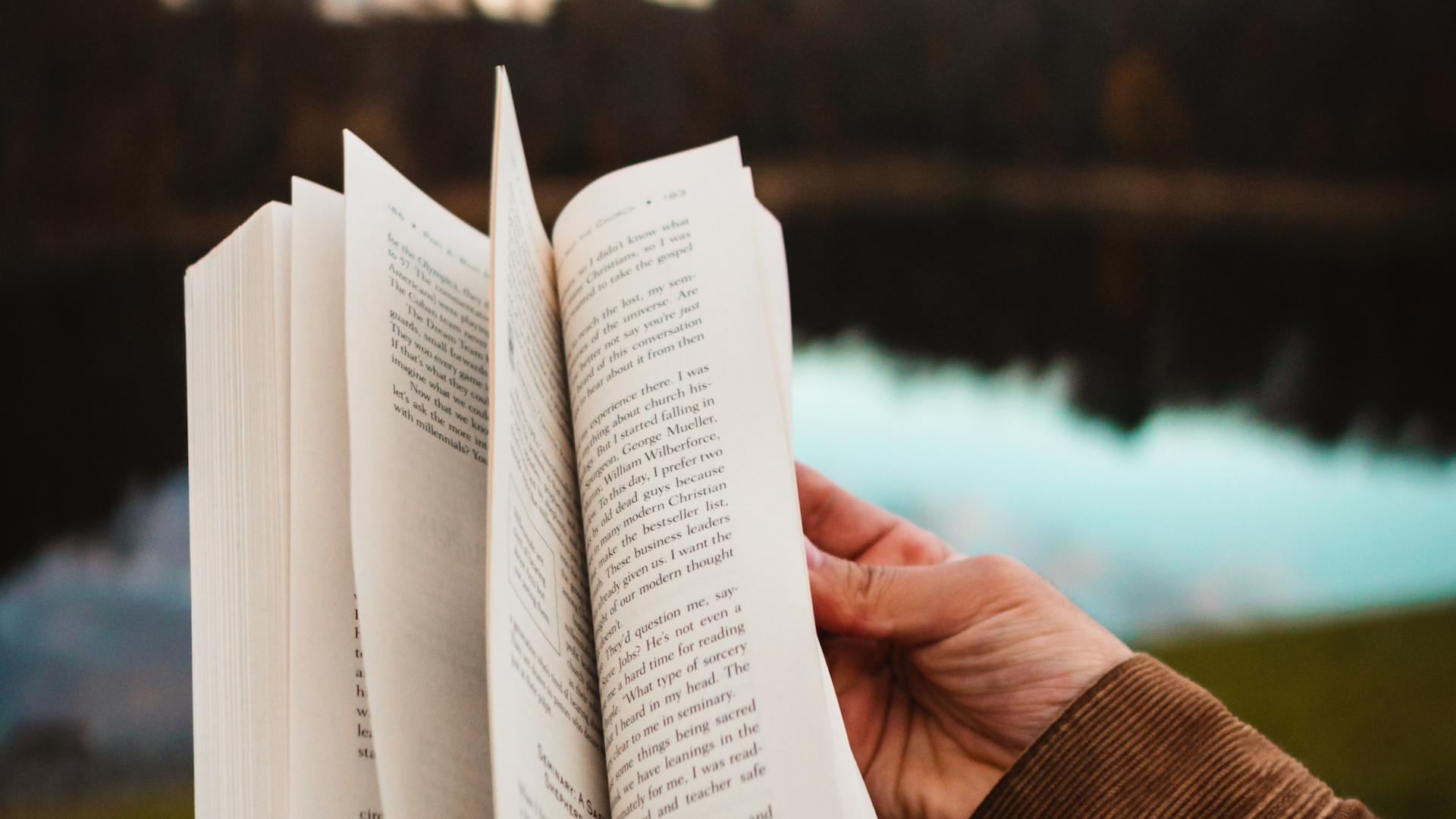 Hands flipping through a book to the story resolution in front of a lake - Photo by whereslugo on Unsplash